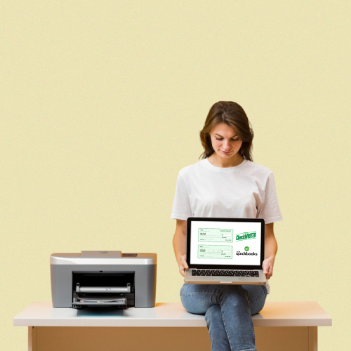 A Woman Sitting at a Desk with a Laptop and Printer, Using QuickBooks Check Printing