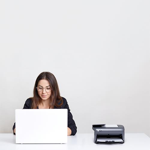 A Woman Check Writing on a Laptop in Front of a Printer