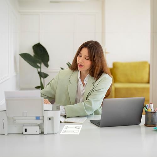 A Woman Working at a Desk with a Printer and Laptop Using Free Payroll Check Printing Software