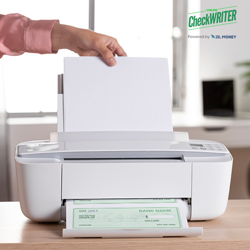 A Person Inserts a Blank Sheet into a White Printer on a Desk, Which Is Printing Checks, Demonstrating How to Take Control of Your Finances by Easily Printing Checks at Home.