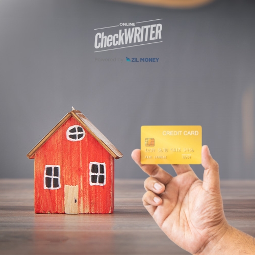 A Person Holds a Credit Card Close to a Miniature Wooden House Model on a Table Symbolizing Securely Pay a Mortgage with a Credit Card Online