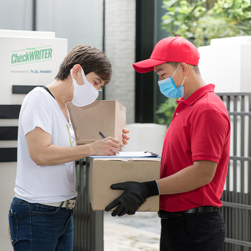 A Delivery Boy Hands a Checks by Mail Package to a Customer. The customer Signs a Clipboard