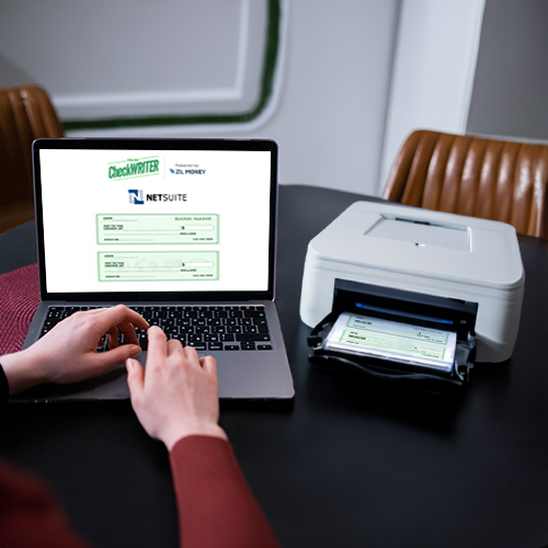 A Man Using A Laptop and a Printer on the Table. Currently, NetSuite Check Printing Is Underway