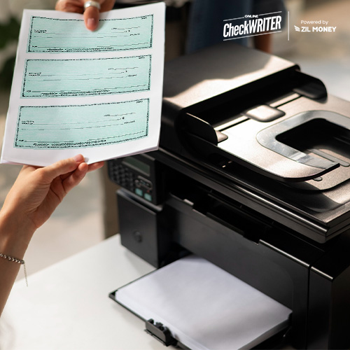 A Person Standing Next To a Regular Printer Holding Checks. Print Checks Online and Eliminate the Need to Order Business Checks Online