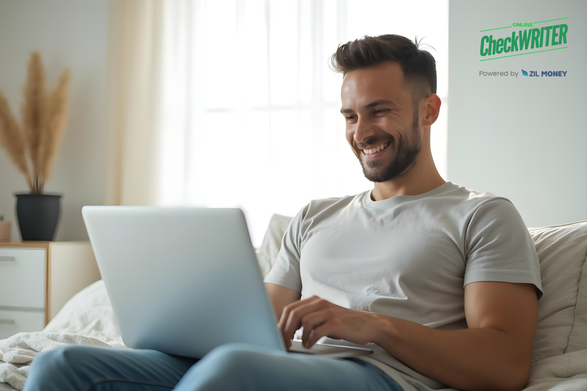 Netsuite Integration Being Managed by a Happy Man Working on a Silver Laptop in a Sunlit Bedroom with Soft Curtains and Minimalist Decor.