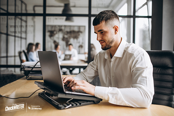 Oracle NetSuite Integration in Use by a Young Professional Working on a Laptop at His Desk, While a Finance Team Collaborates in a Modern Glass-Walled Office.