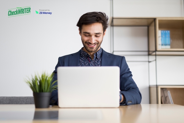 A Young Man Smiling at His Laptop While Managing Bulk Payment Securely and Quickly for His Business.