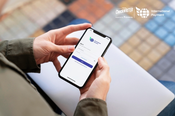 Person holding a smartphone showing a login screen for an app used to manage international payments.