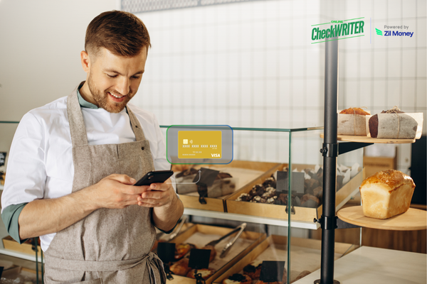 A smiling restaurant worker checking his phone near a display of baked goods, illustrating the convenience of Restaurant Employee Cards.