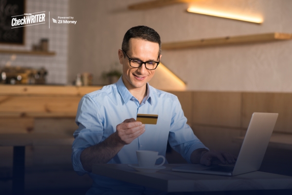 How Payroll by Credit Card Supports Financial Stability for Businesses Smiling man at a cafe using a laptop for Payroll by Credit Card, highlighting convenient business stability.