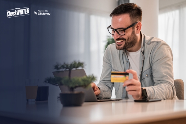 How Paying Business Bills with a Credit Card Can Help Improve Cash Flow Timing A smiling man uses his laptop to pay business bills with a credit card, showcasing easy financial management.