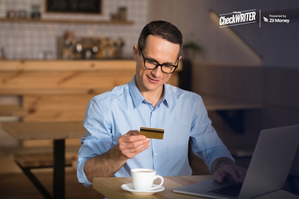 Reasons to Pay Employees with Your Credit Card – Without Changing How They Get Paid Man at a laptop holds a card to Pay Employees with Your Credit Card, showing a convenient way to manage payroll.