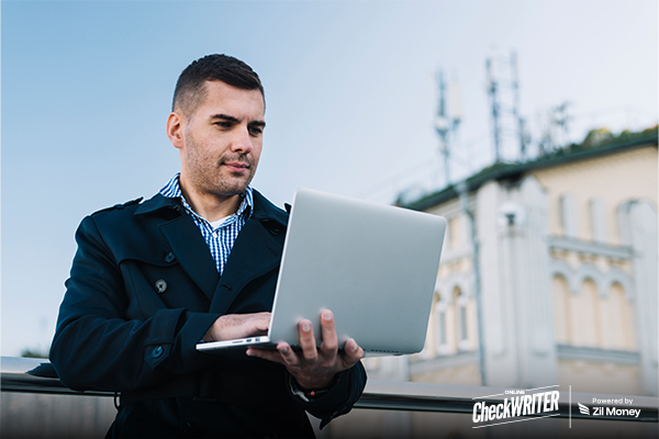 Bulk Payment Problems Killing Your Finance Team’s Friday – And the Fix That Improves the Process A man in a coat stands outdoors using a laptop to Send Bulk payments for improved business efficiency.