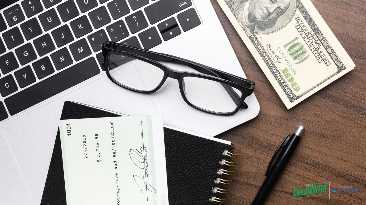How to Create a Deposit Slip Online – Hero Image Desk scene with cash, a personal check, a laptop keyboard, and glasses representing creating a deposit slip online with OnlineCheckWriter.com